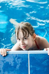 Young girl posing in pool holding the edge.