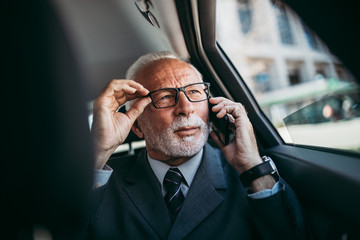 Good looking senior business man sitting on backseat in luxury car. He using his smart phone and reacting emotionally. Transportation in corporate business concept.