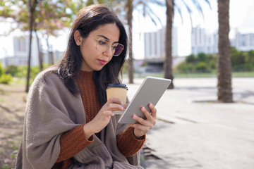 Serious pretty woman using tablet computer outdoors