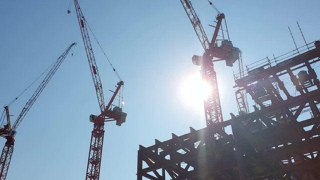 Construction cranes on the background of the blue sky and the bright sun, which is hidden behind the construction crane