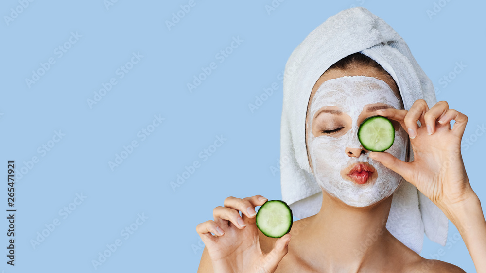 Wall mural beautiful young woman with facial mask on her face holding slices of cucumber. skin care and treatme