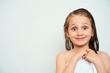 Little preschool girl with wet hair photographed against white background wrapped in white towel...