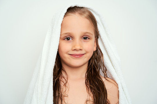 Smiling little preschool girl with wet hair photographed against white background wrapped in white towel