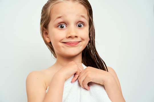 Little preschool girl with wet hair photographed against white background wrapped in white towel with surprised expression on the face