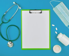 paper holder with empty white sheets, medical stethoscope, pills on a blue background, top view, space for writing a prescription