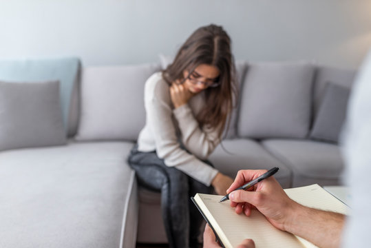 Cropped image of depressed man at the psychotherapist. Doctor is making notes while listening to his patient. Woman at therapy session. Attentive psychologist.