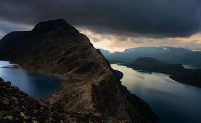 Dramatic Mountain Landscape. Sunrise after a storm. Dark stormy clouds. Majestic mountain ridge and ferry boat making its way through glacier lake. Besseggen, Norway