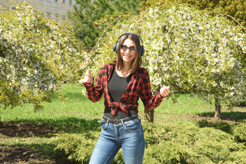 Happy girl listening to music on headphones and dancing in the park