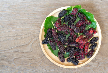 Close up of mulberry with a green leaves on the wooden plate on wooden table. Mulberry this a fruit and can be eaten in have a red and purple color and delicious and sweet nature.