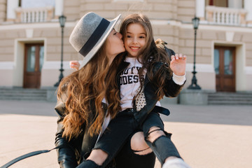 Joyful brunette girl with lovely face expression in stylish jeans with holes sitting on mom's knee...