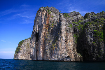 Fototapeta premium Boat trip along the coast line of tropical island Ko Phi Phi along impressive rock formations under blue sky