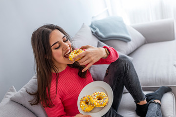 Woman is eating tasty sugary donuts. Portrait of beautiful young woman eating donuts at home. Woman...