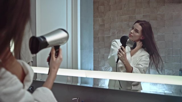 Female blow drying hair in bathroom