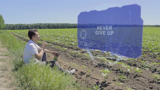 Man is working on HUD holographic display with text Never give up on the edge of the field. Businessman analyzes the situation on his plantation. Scientist examines future technology