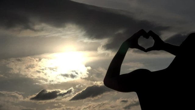 ein Mann bilden bei Sonnenuntergang am See ein Herz mit den H&auml;nden	