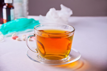 Cup of tea with lemon, thermometer, medicaments and pills on white table. Disease concept.