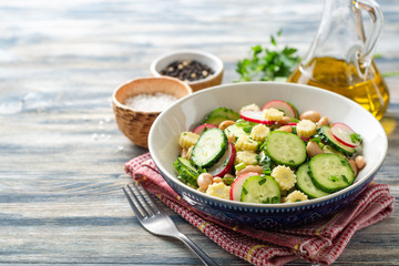 Healthy vegetable salad with cucumber, radish, beans, mini corn and herbs on rustic wooden background. Selective focus.