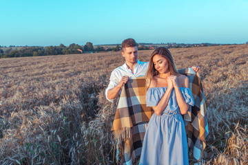 Happy young couple, man and woman, summer covering rug. Wheat field, outdoor recreation in village. Emotions tenderness, care, affection, love, respect. Concept of romantic love, date and family.