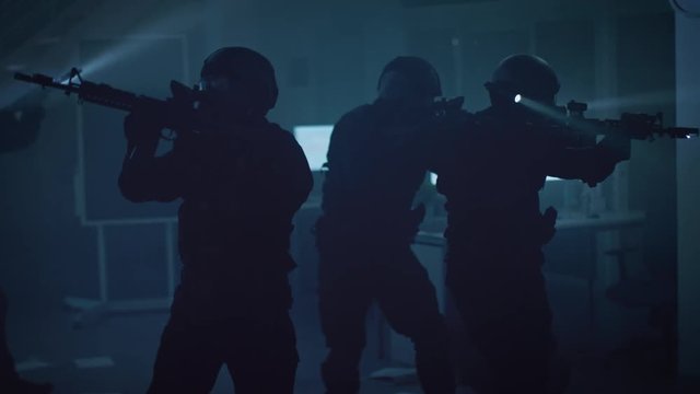 Masked Team of Armed SWAT Police Officers Slowly Move in a Hall of a Dark Seized Office Building with Desks and Computers. Soldiers with Rifles and Flashlights Surveil and Cover Surroundings.