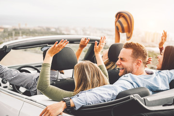 Group of friends having fun in convertible car during road trip at sunset - Young travel people...