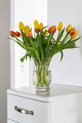 Bouquet of red and yellow tulips on a white sideboard