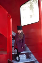 Foto auf Leinwand Little cheerful girl near the red English bus in a beautiful coat and a hat. Child's journey. School bus.  London red bus. Spring.  With the International Women's Day. Since March 8! © stock_studio