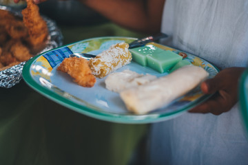 Young girl holding a plate of consisting most of filipino desserts - pichi pichi or known as grated cassava, gelatin, maja or known as coconut pudding, fresh lumpia, together with fried chicken. 