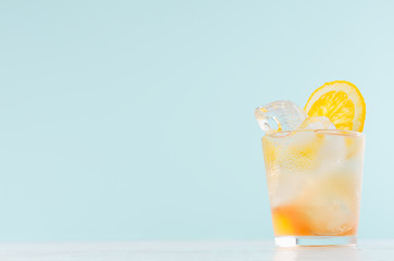 Cold oranges beverage in wet shot glass with pieces orange, ice cubes on elegant soft light green background, copy space.