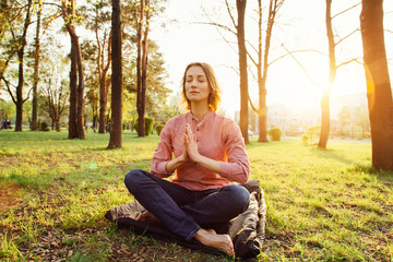Fototapeta premium Young woman is meditating in a city park on a sunset background.