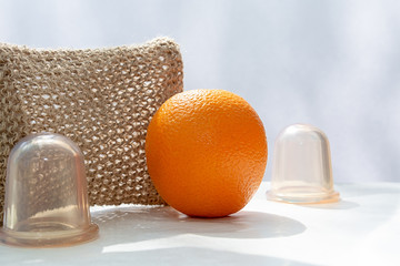 An orange is on the table and next to it are vacuum cans and a mesh washcloth made from natural...