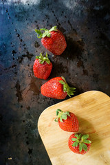 Ripe, red strawberries with water drops splash and wooden cutting board on dark background. Top view.