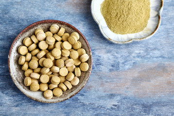 Bio Green BARLEY GRASS tablets and powder. Concept for a healthy dietary supplementation. Rustic wooden background. Top view. Copy space. 