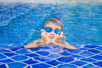 cute little boy feel happy play and swimming at swimming pool , sunny day and soft focus.