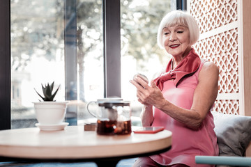 Beaming stylish old lady in pink top checking her makeup