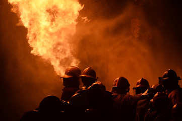 Fototapeta na wymiar firefighters with fire hose fight with fire at night