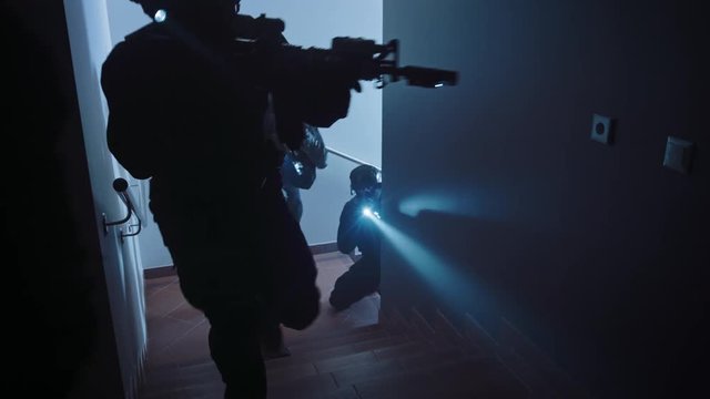 Masked Squad of Armed SWAT Police Officers Move Up the Stairs in a Corridor of an Office Building. Soldiers with Rifles and Flashlights Move Forwards and Cover Surroundings. 