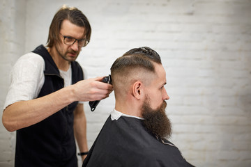 Brutal guy in modern Barber Shop. Hairdresser makes hairstyle a man with a long beard. Master hairdresser does hairstyle with hair clipper