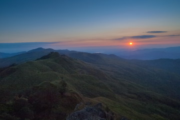 Mountain view morning above many hills and green forest around with soft fog with colorful red sun light in the sky background, sunrise at top of Phu Langka Forest Park, Phayao, Thailand.