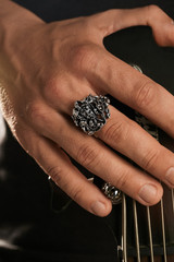 Cropped closeup shot of man's hand, touching headstock of guitar. The guy is wearing signet with...