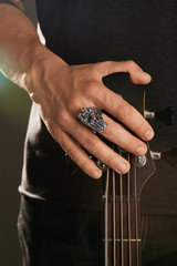 Cropped shot of man's hand, touching headstock of guitar. The guy is wearing signet-ring in view of...
