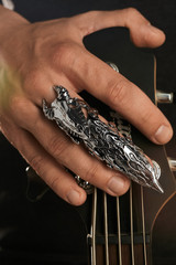 Cropped closeup shot of man's hand, touching headstock of guitar. The guy is wearing claw-ring with...