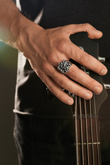 Cropped shot of man's hand, touching headstock of guitar. The guy is wearing massive signet-ring...