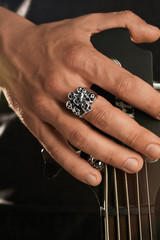 Cropped closeup shot of man's hand, touching headstock of guitar. The guy is wearing signet-ring with blacking in view of skulls. The man is wearing black clothes, posing against dark background.