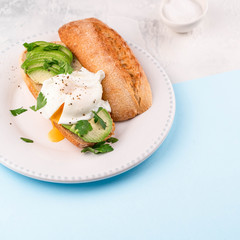 poached egg and avocado on bread on white plate, on blue paper and white backdrop