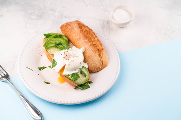 poached egg and avocado on bread on white plate, on blue paper and white backdrop