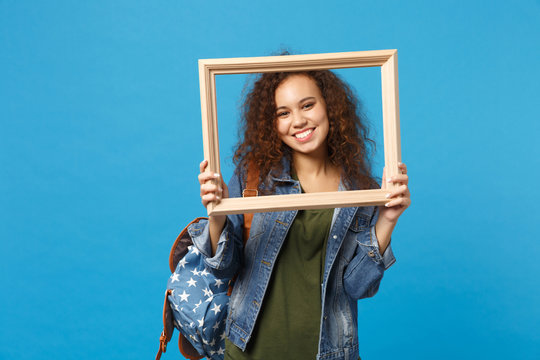 Young african american girl teen student in denim clothes, backpack hold frame isolated on blue wall background studio portrait. Education in high school university college concept. Mock up copy space