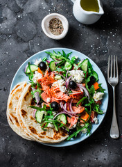 Greek salad with baked salmon on a dark background, top view. Healthy mediterranean diet food