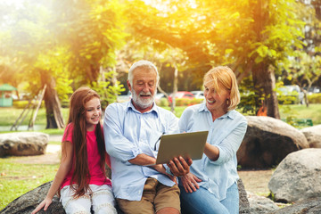 Happy grandfather and grandmother using notebook or laptop with granddaughter in summer day