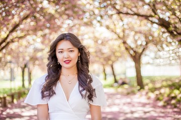 A young beautiful Asian woman in a white dress walks in a flowered park. Sakura. Blooming trees.