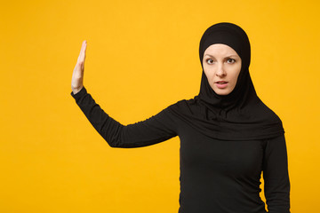 Sad upset crying confused young arabian muslim woman in hijab black clothes posing isolated on yellow wall background, studio portrait. People religious Islam lifestyle concept. Mock up copy space.